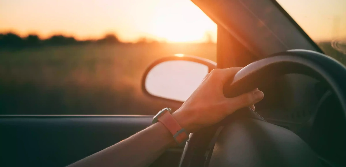 woman-hands-on-steering-wheel-sunset